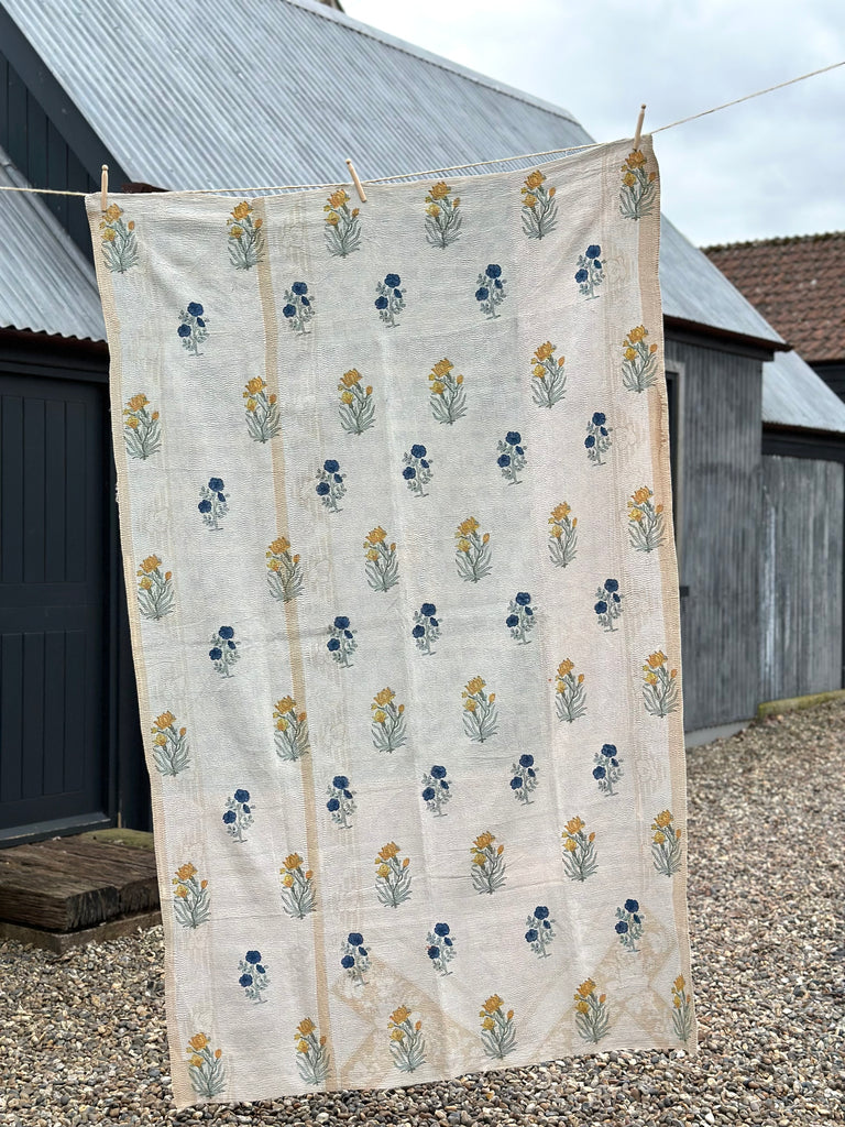 cream coloured indian kantha quilt hangs outside with blue and yellow flower pattern