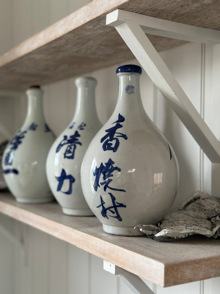 White ceramic bottles with blue text on a wooden shelf