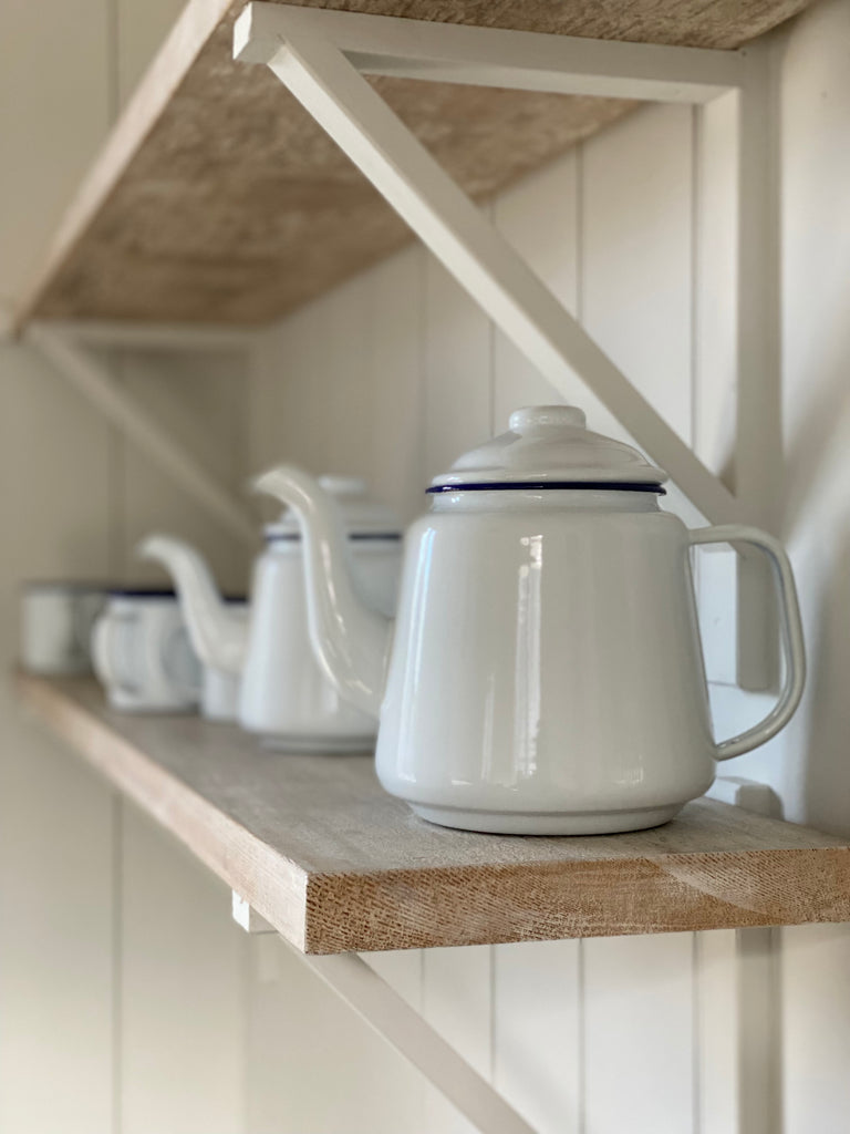 white enamel teapots with a blue rim detail around the join where the lid sits. all of the teapots in the photo are sat on a shelf.