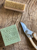 cube of green soap with a speckled coffee surface. pictured next to a nail brush and secateurs.