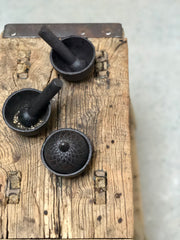 Small, black, cast iron pestle and mortars, shown crushing peppercorns. Mini lidded, black, cast iron, acorn style pot.