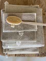 A stack of linen towels in natural colour. Each towel has a hanging loop in matching natural colour. Displayed with a beech back brush, hand loop on the back and long handle.