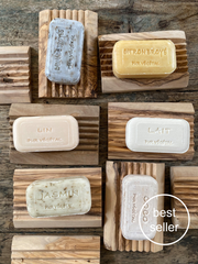 rectangular, hand made french soaps, engraved with their names. each soap is displayed on top of a ridged olive wood soap dish.